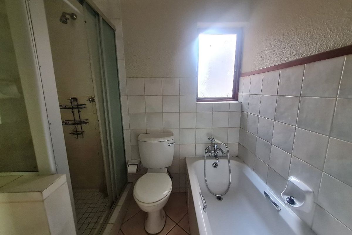 A dated bathroom featuring a bathtub, separate shower enclosure, and toilet with tiled walls and flooring, requiring cosmetic updates.
