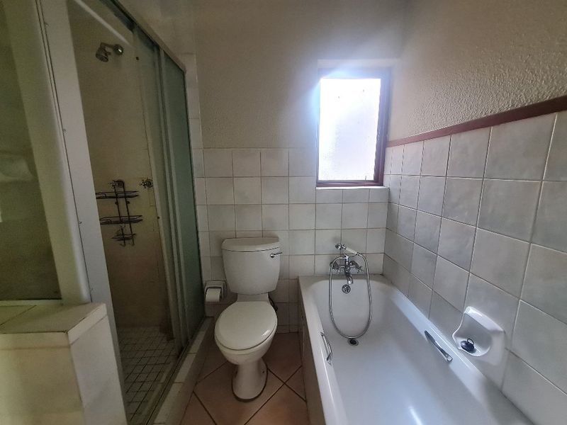 A dated bathroom featuring a bathtub, separate shower enclosure, and toilet with tiled walls and flooring, requiring cosmetic updates.