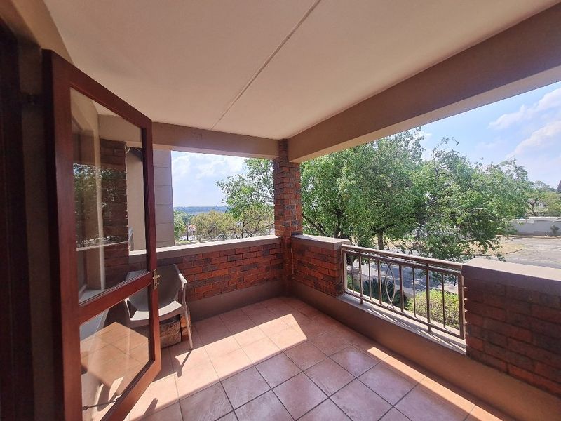 A covered balcony featuring brick walls, tiled flooring, and metal railings, offering an open outdoor space with views of the surrounding area.