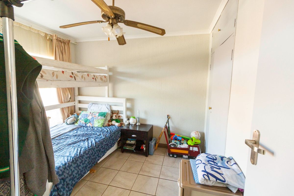 A functional bedroom featuring tiled flooring, a ceiling fan, and built-in storage cupboards.