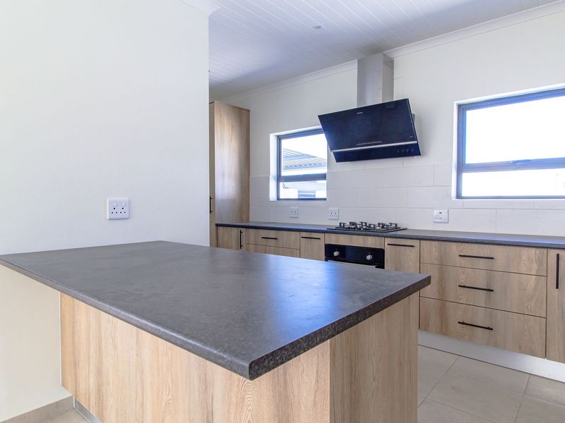 Modern kitchen featuring light wood cabinetry, dark stone countertops, a central island, and integrated stainless steel appliances.