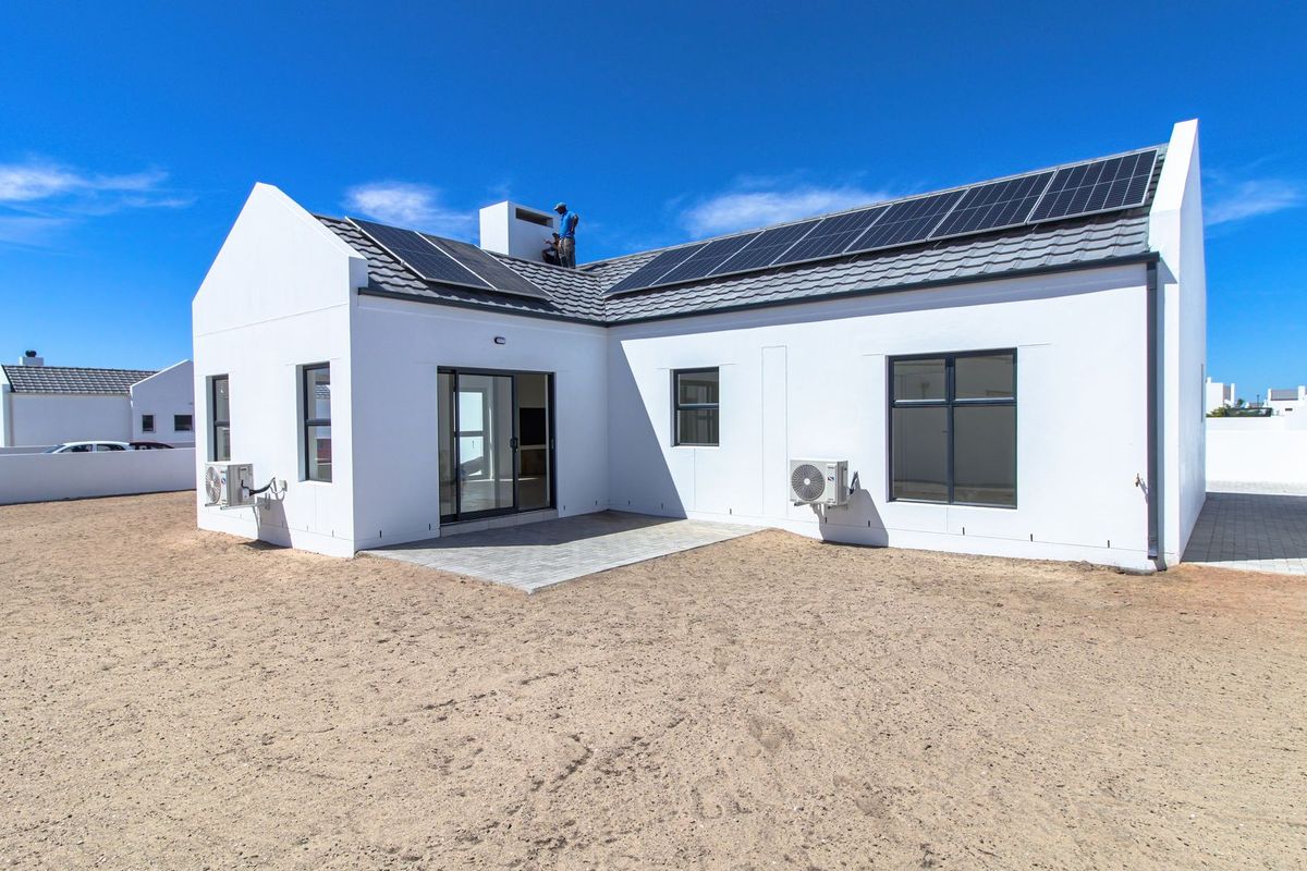 Rear view of a modern house featuring a tiled roof with solar panels, paved patio area, and exterior air conditioning units.
