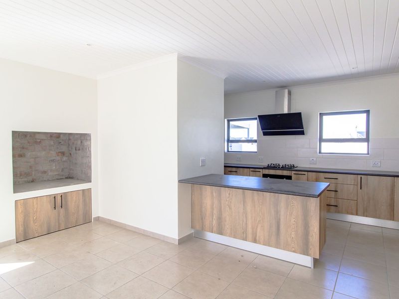 Modern open-plan kitchen and living area featuring wood-finish cabinetry, stone countertops, a gas hob, and a built-in fireplace with tiled flooring throughout.
