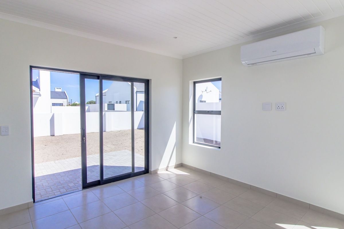 A bright, empty living room featuring tiled floors, a split-system air conditioner, and sliding glass doors leading to an outdoor patio area.