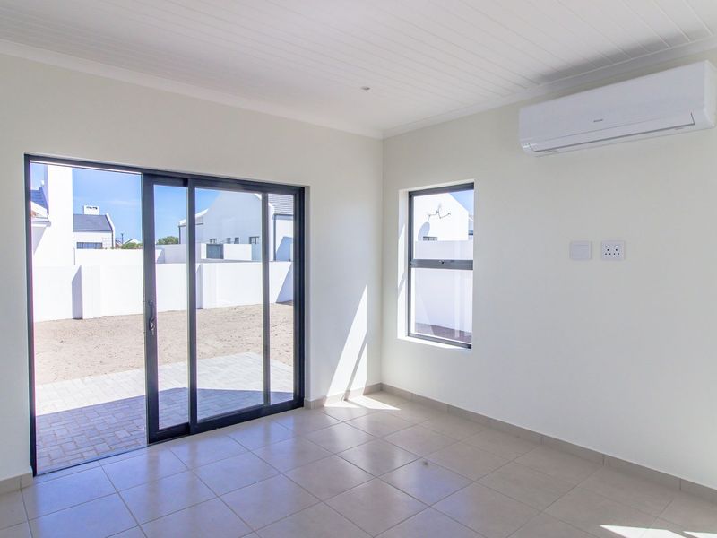 A bright, empty living room featuring tiled floors, a split-system air conditioner, and sliding glass doors leading to an outdoor patio area.