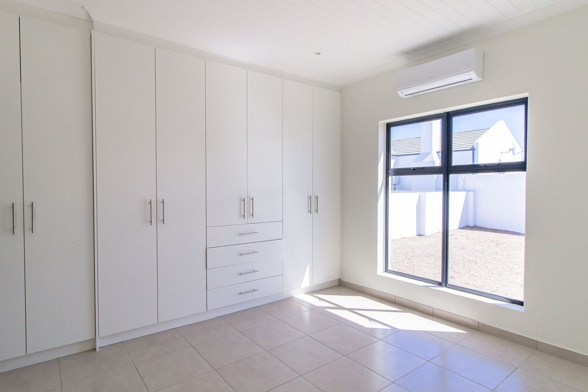 A bright, modern bedroom featuring extensive built-in cupboards, tiled flooring, and a wall-mounted air conditioning unit.