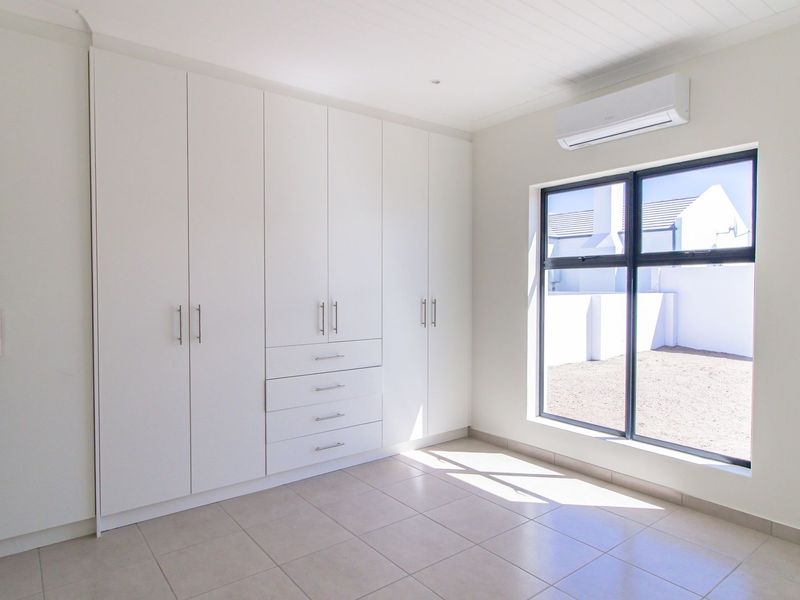 A bright, modern bedroom featuring extensive built-in cupboards, tiled flooring, and a wall-mounted air conditioning unit.