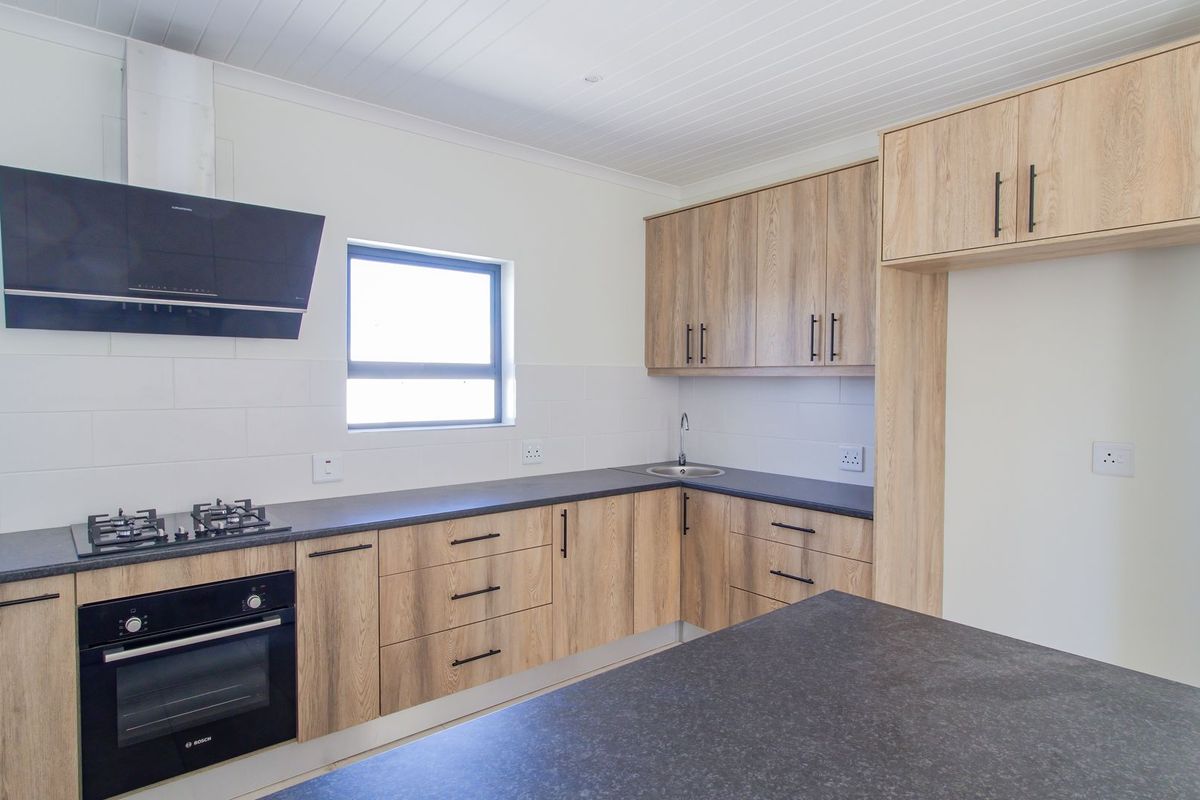 Modern kitchen featuring light wood-grain cabinetry, dark stone-look countertops, built-in gas hob, oven, and extractor fan with a clean, contemporary finish.