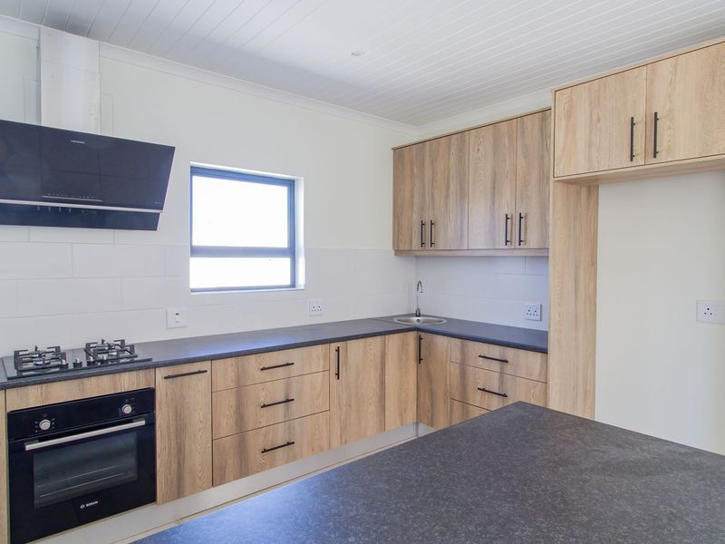 Modern kitchen featuring light wood-grain cabinetry, dark stone-look countertops, built-in gas hob, oven, and extractor fan with a clean, contemporary finish.