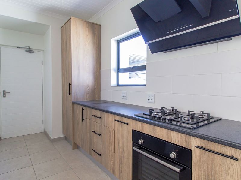 Modern kitchen featuring wood-look cabinetry, dark laminate countertops, a gas hob, built-in oven, and a sleek extractor fan with neutral tiled finishes.