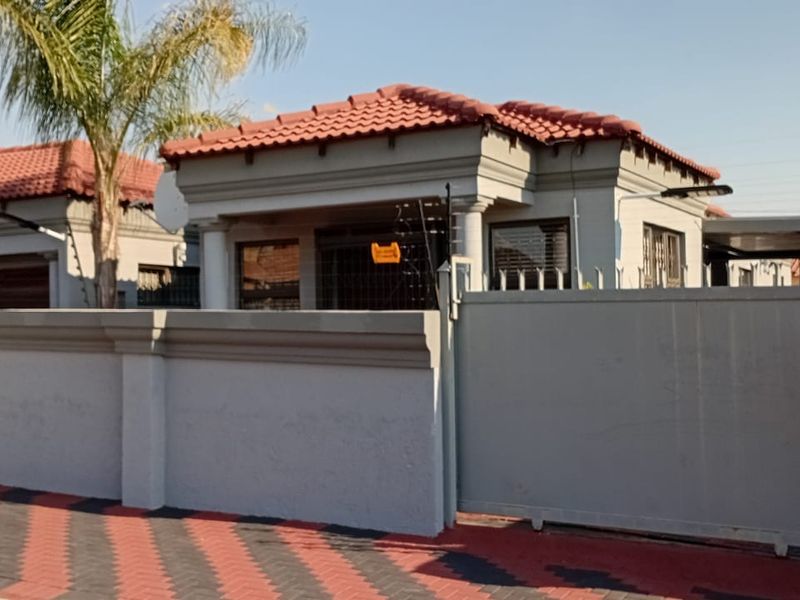 Front view of a well-maintained house featuring a tiled roof, secure perimeter wall with electric fencing, and a paved driveway.