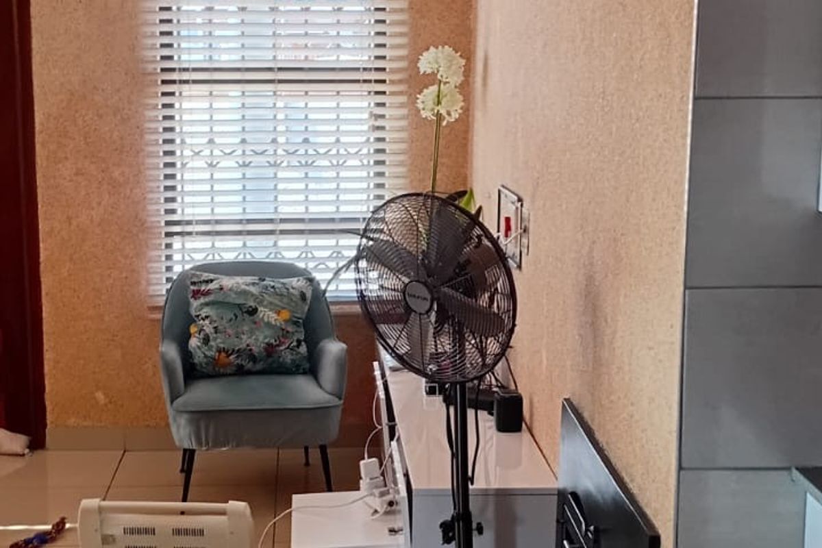 A living area featuring large format floor tiles, textured wall finishes, and a window fitted with venetian blinds.