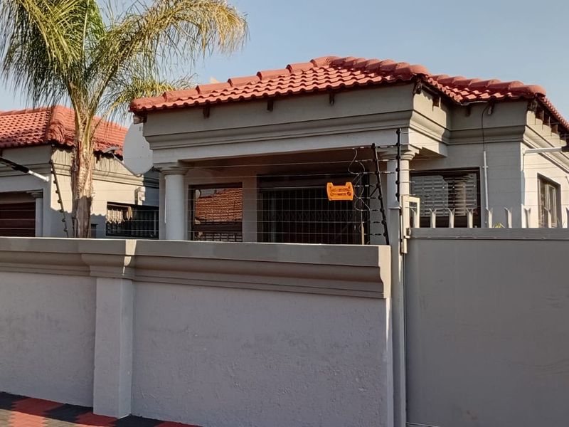 Front view of the property featuring a secure perimeter wall with electric fencing, tiled roof, and a paved driveway entrance.