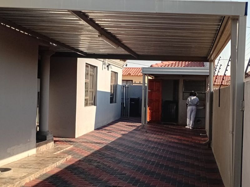 A covered carport area featuring paved flooring and a metal roof structure, providing sheltered parking space alongside the property.