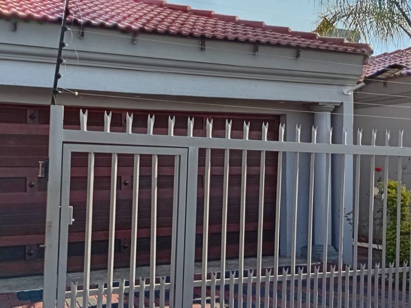 Front elevation of the property featuring a secure metal gate, electric fencing, and a tiled roof garage entrance.