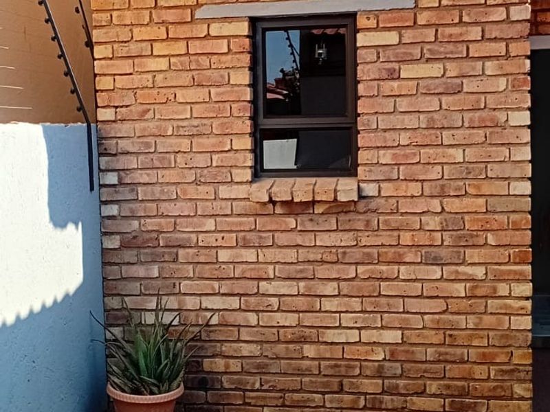A rear exterior view featuring a face brick wall with a thatched roof section, electric fencing, and a paved patio area.