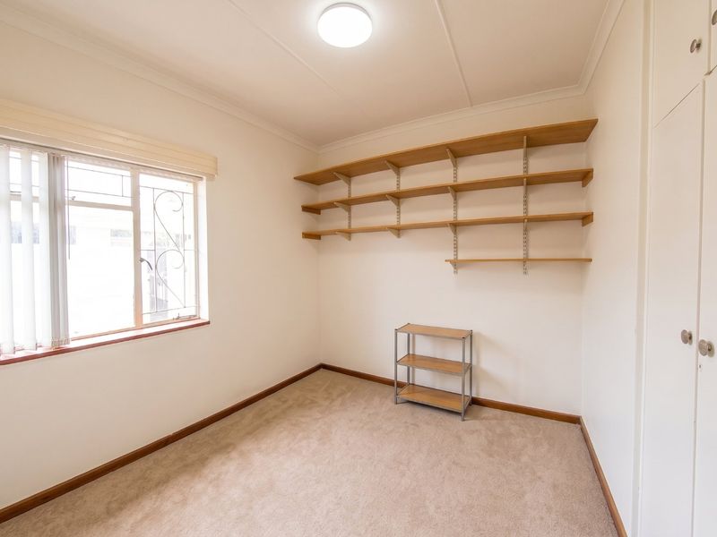 A clean, neutral bedroom featuring built-in cupboards, wall-mounted shelving, and carpeted flooring, offering a versatile space ready for personalization.