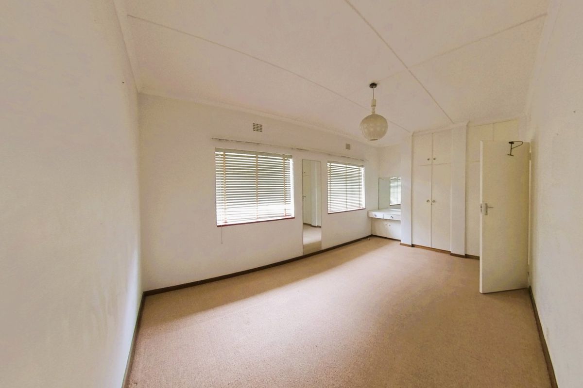 A spacious, empty bedroom featuring built-in cupboards, a vanity area, and venetian blinds, offering a neutral canvas for potential updates.