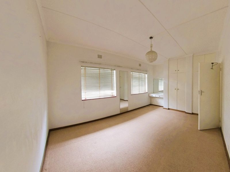 A spacious, empty bedroom featuring built-in cupboards, a vanity area, and venetian blinds, offering a neutral canvas for potential updates.