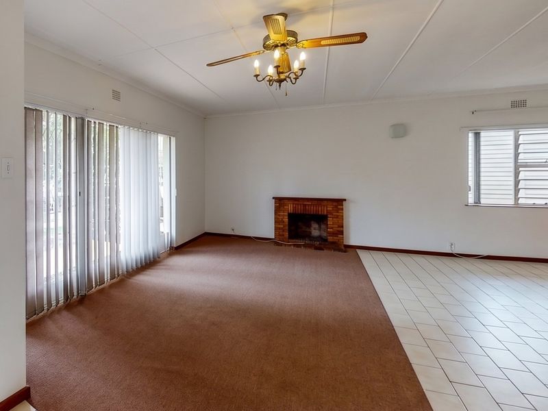 Spacious living area featuring a brick fireplace, ceiling fan, and a combination of carpet and tiled flooring with access to the exterior.