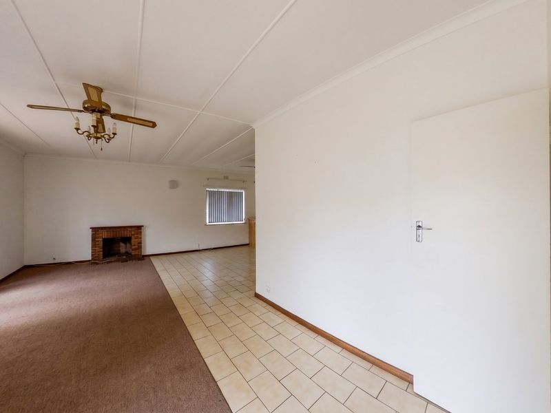 Spacious open-plan living area featuring a brick fireplace, a mix of carpet and tile flooring, and a ceiling fan.