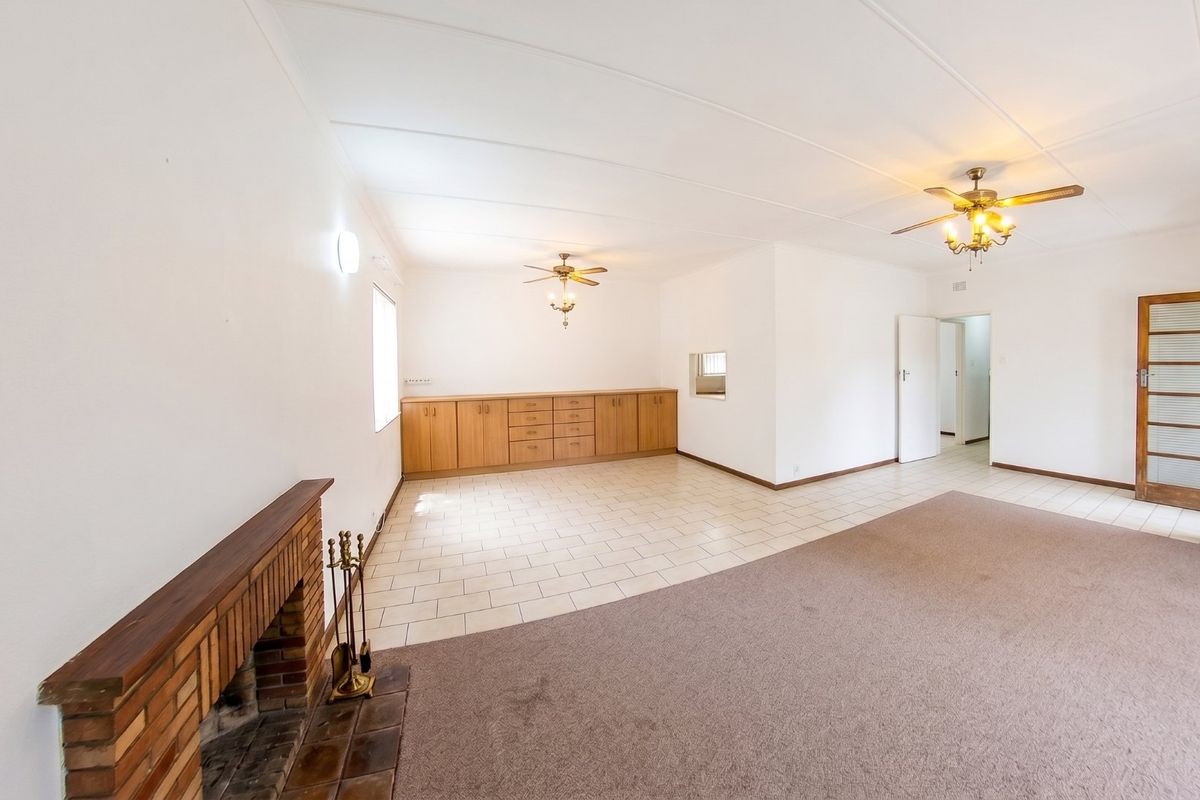 Spacious living area featuring a brick fireplace, built-in cabinetry, ceiling fans, and a combination of tiled and carpeted flooring.
