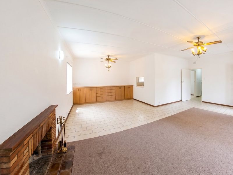 Spacious living area featuring a brick fireplace, built-in cabinetry, ceiling fans, and a combination of tiled and carpeted flooring.