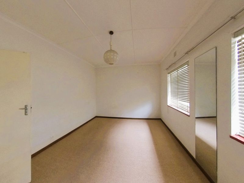 An empty bedroom featuring neutral carpet flooring, a built-in mirror, and venetian blinds on the windows.