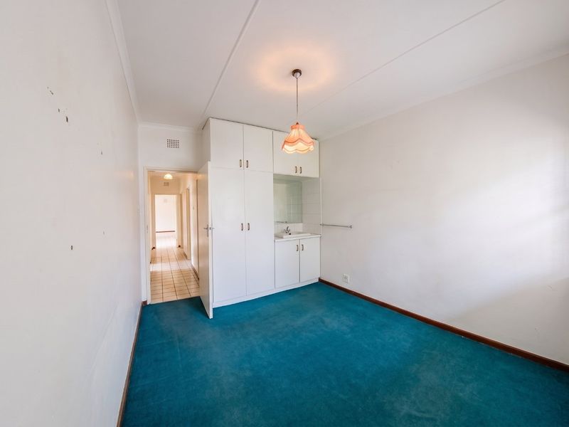 A vacant bedroom featuring built-in cupboards with an integrated vanity basin, blue carpeting, and security bars on the windows.