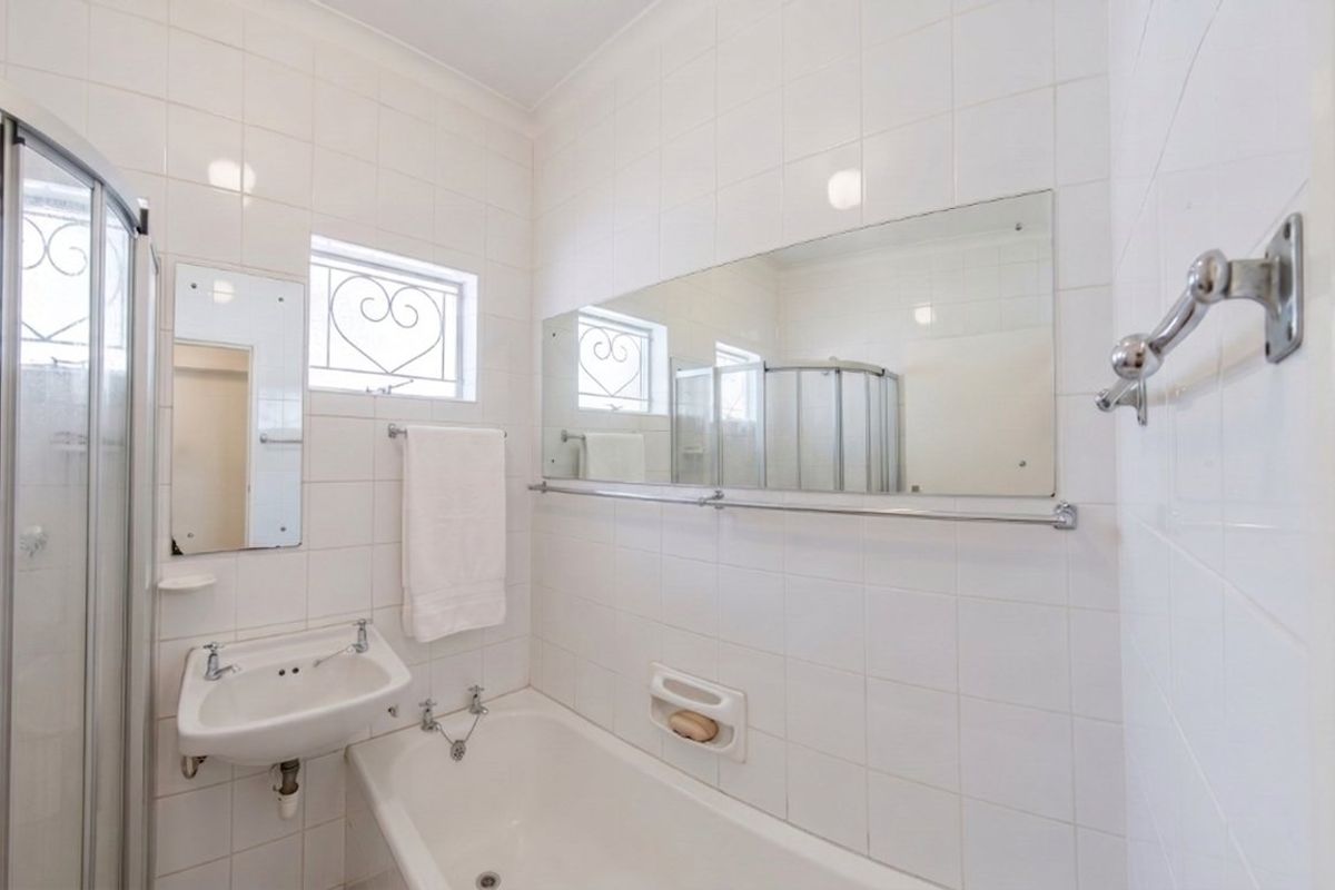 A functional bathroom featuring a shower enclosure, bathtub, wall-mounted basin, and full-height wall tiling, offering a clean and practical layout.