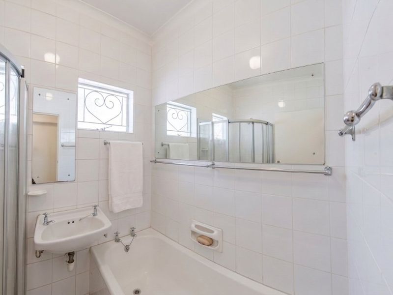 A functional bathroom featuring a shower enclosure, bathtub, wall-mounted basin, and full-height wall tiling, offering a clean and practical layout.