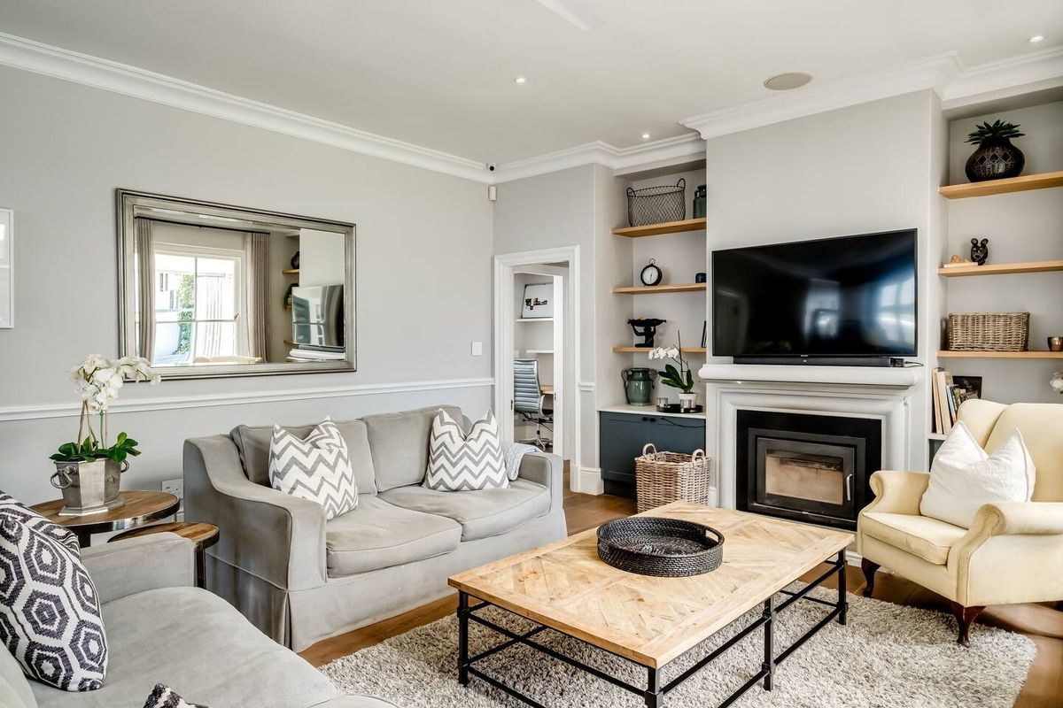 A well-appointed living room featuring a fireplace, built-in shelving, crown molding, and elegant wainscoting, finished with high-quality hardwood flooring.