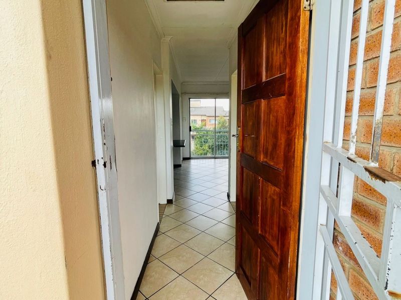 A view through the entrance into a tiled hallway leading towards a balcony, featuring a wooden door and security gate.