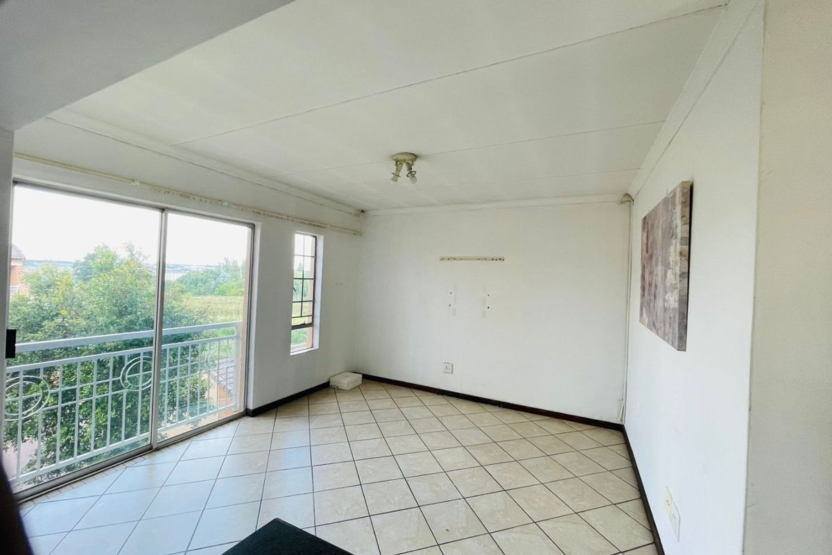 An empty living room featuring tiled flooring and a sliding glass door leading to a balcony with exterior views.