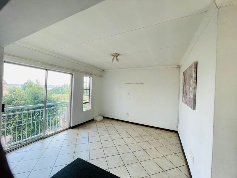 An empty living room featuring tiled flooring and a sliding glass door leading to a balcony with exterior views.