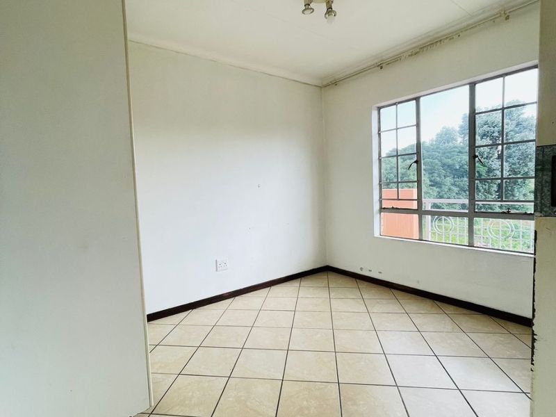 A vacant bedroom featuring tiled flooring, a built-in cupboard, and a large window providing natural light and exterior views.
