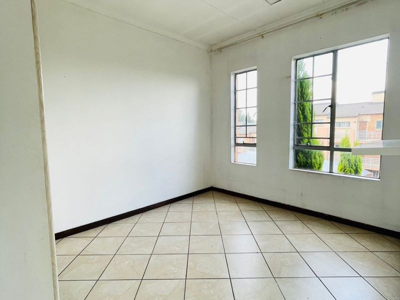 An empty, sunlit living area featuring neutral tiled flooring and steel-framed windows, offering a blank canvas for renovation and interior design.