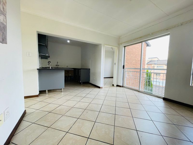 Open-plan living area featuring tiled flooring, a compact kitchen with built-in cabinetry, and a sliding door leading to a balcony.