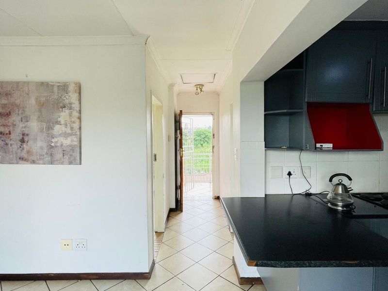 Open plan kitchen area featuring dark cabinetry, tiled flooring, and a direct view through the hallway to the exterior balcony.