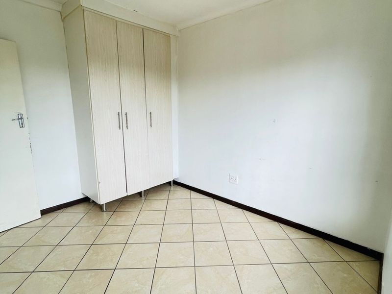 A vacant bedroom featuring neutral tiled flooring and a built-in wardrobe, providing a clean and functional space ready for personalization.
