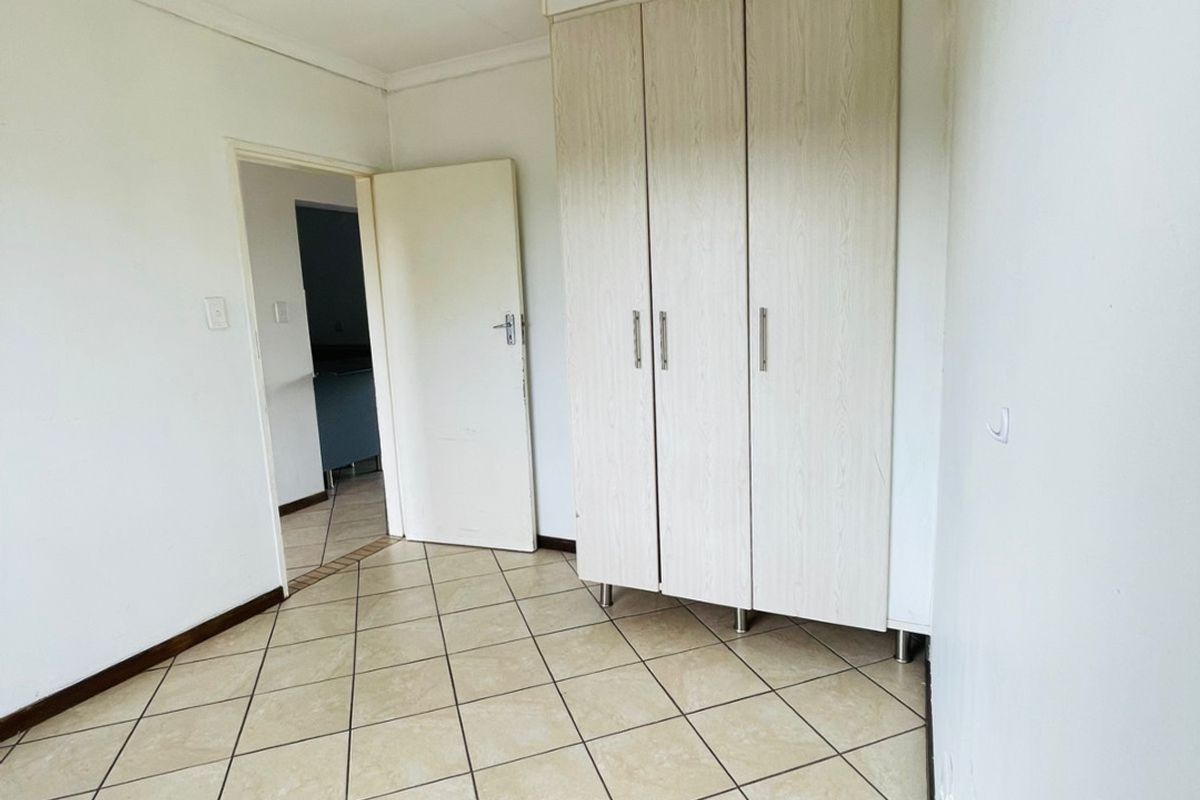 A bright, empty bedroom featuring neutral tiled flooring and built-in cupboards, offering a clean and versatile space ready for personalization.