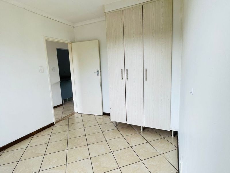A bright, empty bedroom featuring neutral tiled flooring and built-in cupboards, offering a clean and versatile space ready for personalization.