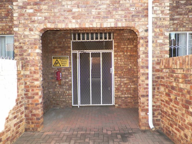 A covered entrance area featuring exposed brickwork, a security gate, and paved flooring, equipped with a wall-mounted fire extinguisher.