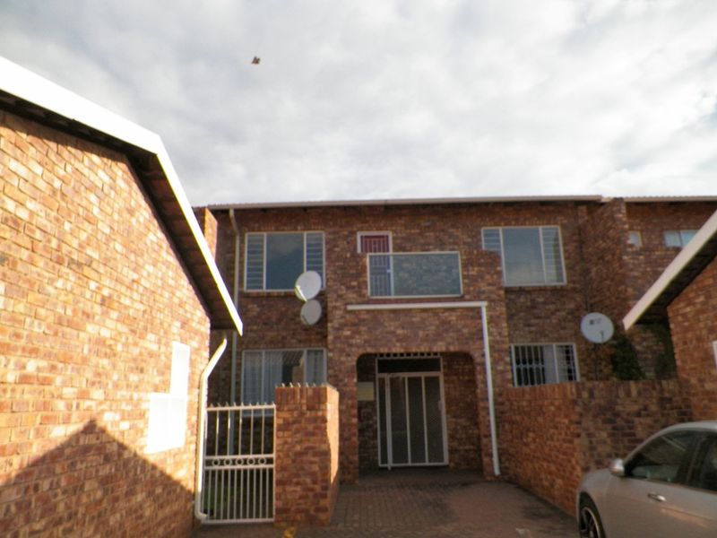 Front elevation of a face brick apartment complex featuring a covered entrance, security gates, and a small balcony.