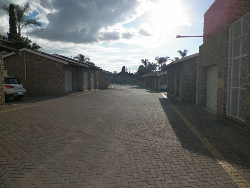 A view of the complex driveway featuring multiple face brick garage units with roller shutter doors and paved access.