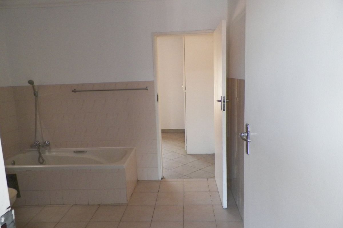 A functional bathroom featuring a built-in bathtub with a handheld shower attachment and neutral tiled finishes.
