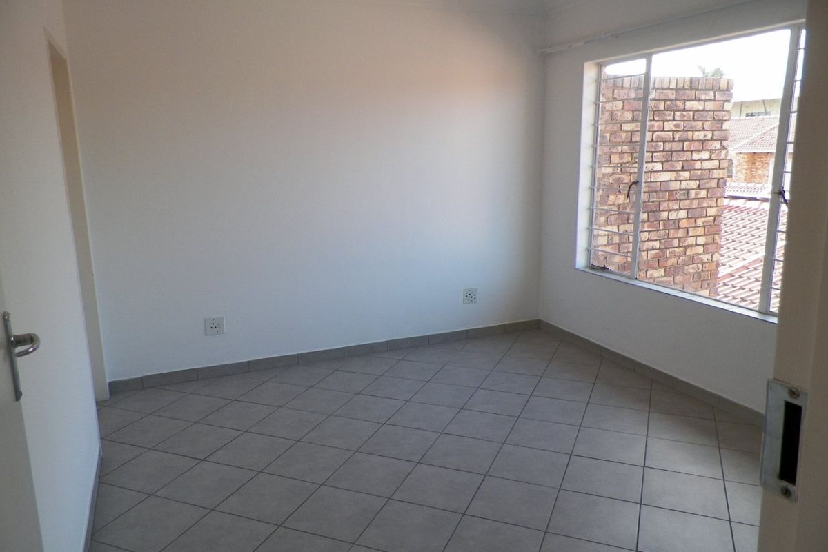A clean, empty bedroom featuring neutral tiled flooring, white walls, and a window fitted with security bars.