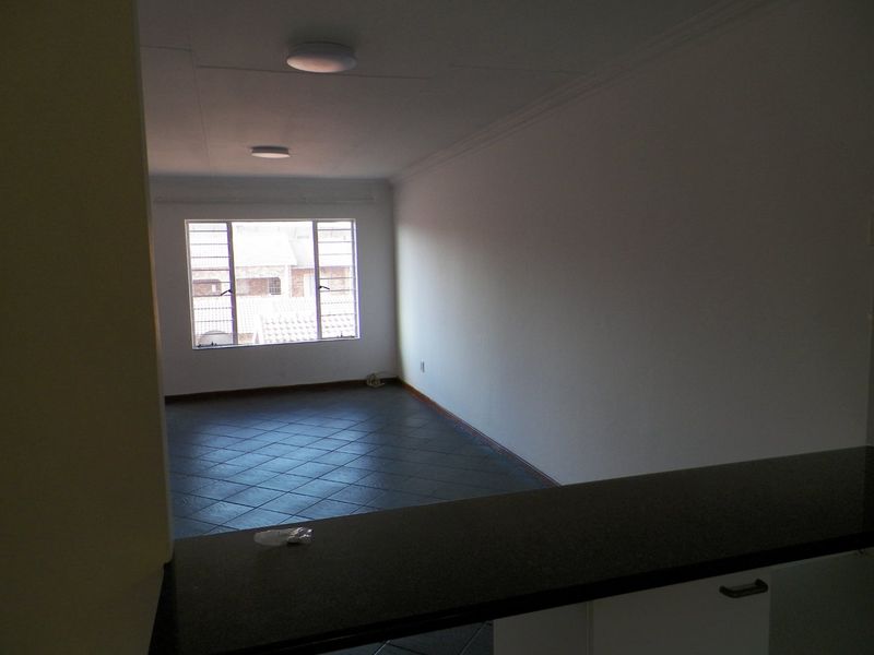 An empty open-plan living area featuring dark tiled flooring, a breakfast bar, and natural light from a window with security bars.