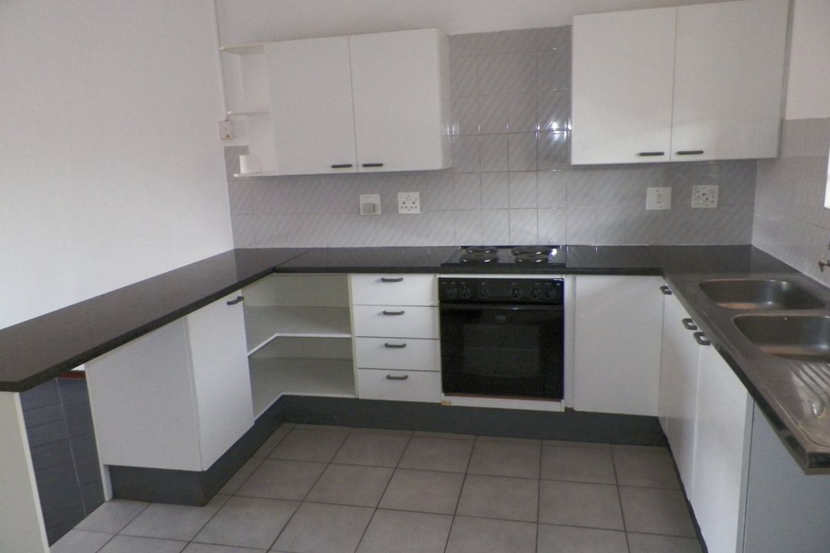 A functional, empty kitchen featuring white cabinetry, dark countertops, a built-in oven with electric hob, and a double stainless steel sink.