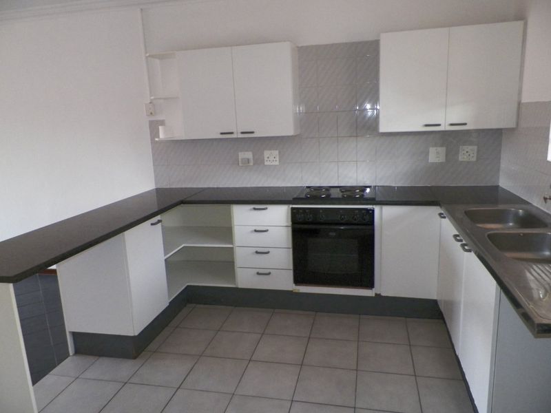 A functional, empty kitchen featuring white cabinetry, dark countertops, a built-in oven with electric hob, and a double stainless steel sink.